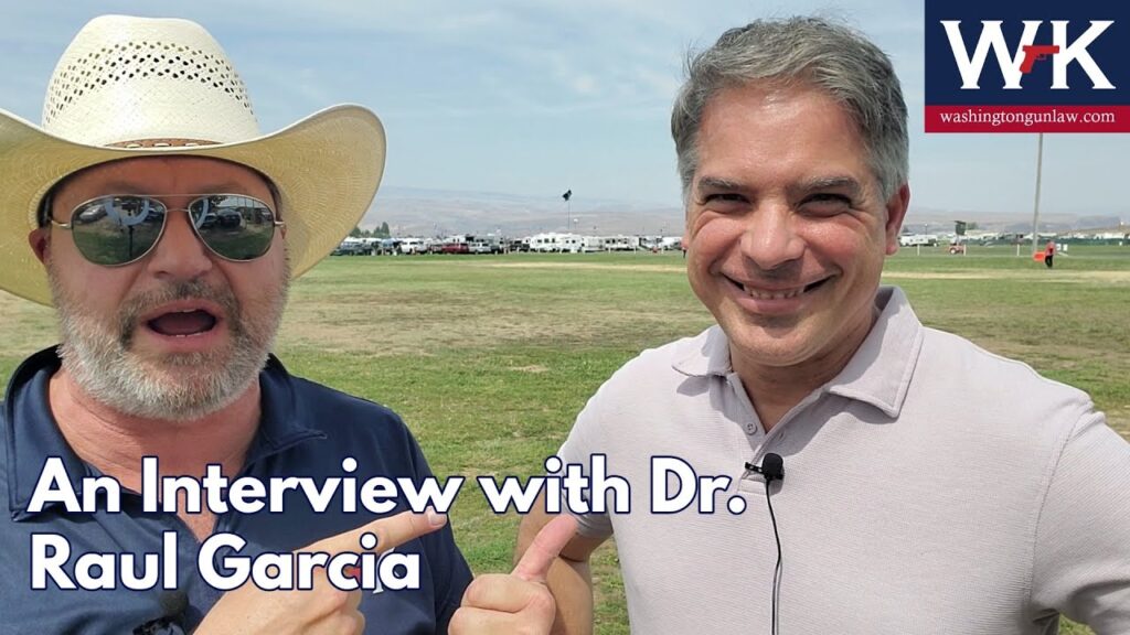 Two men standing in a grassy field, one wearing a hat and sunglasses, pointing towards the other, who is smiling. Text reads "An Interview with Dr. Raul Garcia." Logo in the top right corner with the letters "WK.