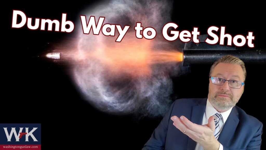 A man in a suit gestures with one hand in front of a large bullet being fired. The text above reads, "Dumb Way to Get Shot." The image has a logo in the bottom left corner with the initials "WJK" and a website URL.