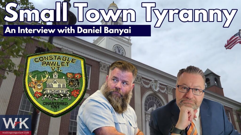 Two men are pictured in front of a large building with a clock tower. Text reads, "Small Town Tyranny: An Interview with Daniel Banyai." The image includes a Pawlet, Vermont constable patch and WK logo. An American flag is in the background.