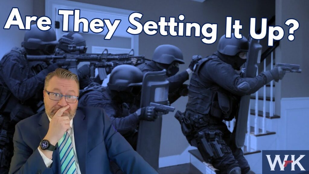 A man in a suit with a thoughtful expression sits in the foreground. Behind him, heavily armed law enforcement officers in tactical gear are positioned. The text "Are They Setting It Up?" is prominently displayed at the top.