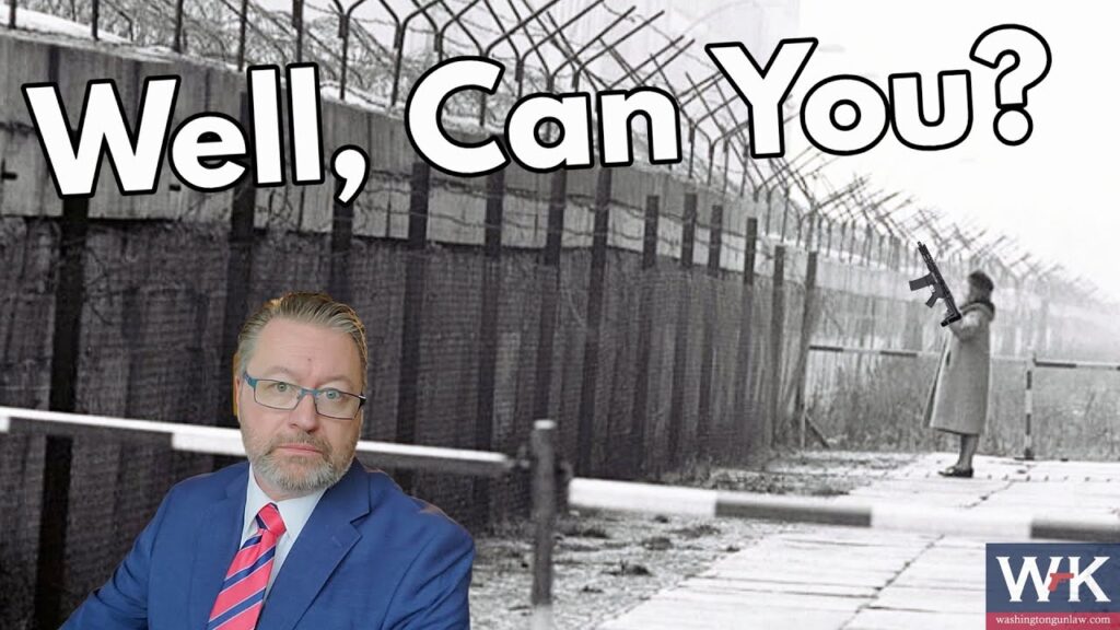 A man in a suit with a pink-striped tie stands in front of a black-and-white photo of a person holding a gun by a barbed wire fence. Text reads "Well, Can You?" The bottom right has a logo with "W↑K" and a URL.