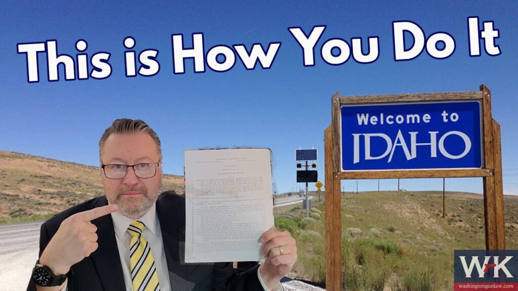 A man in a suit and tie points to a document he is holding. He stands beside a road sign that reads "Welcome to Idaho" under a blue sky. Text at the top says "This is How You Do It.