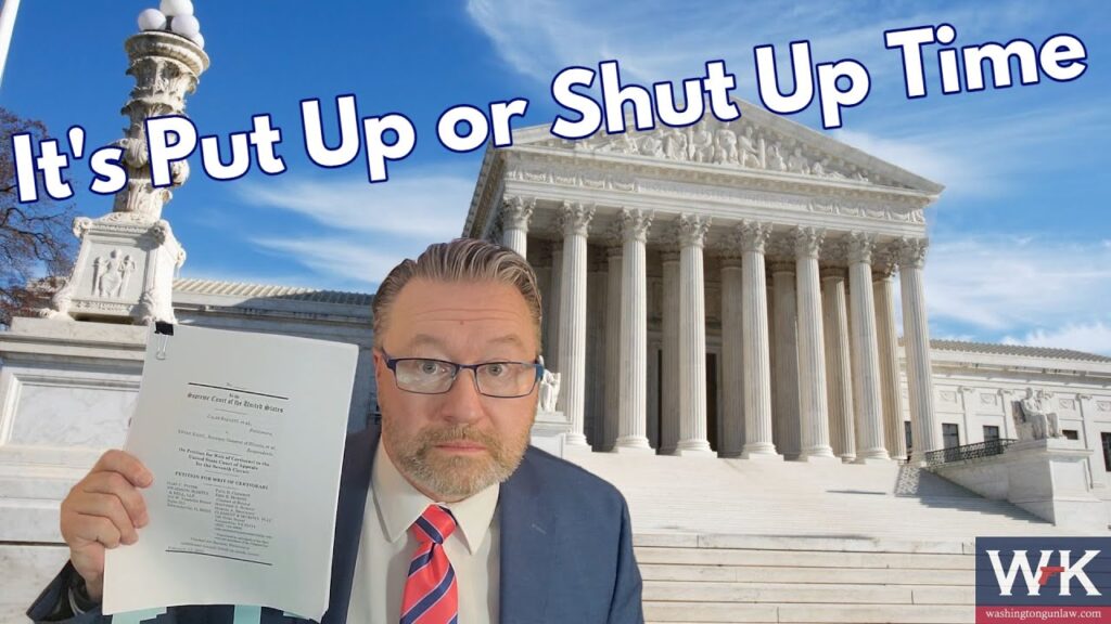 A man in a suit and glasses holds up a document in front of a large, classical building with columns, resembling a courthouse. The text on the image reads, "It's Put Up or Shut Up Time.