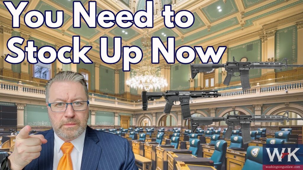 Man in a suit and tie points forward in an empty assembly hall with rifles displayed. Text reads, "You Need to Stock Up Now." Logo in the bottom right corner.
