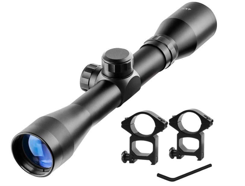 A black rifle scope with blue-tinted lens, featuring adjustment knobs on the top and sides. Next to it, two black mounting rings and an Allen wrench are displayed on a white background.