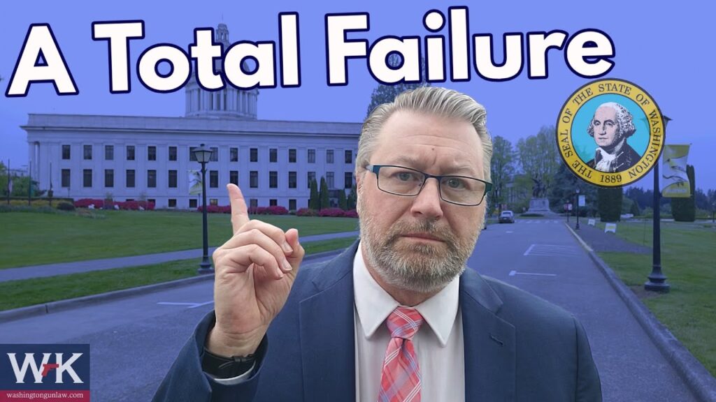 A man in a suit and glasses points upwards with an expression of concern. The background features a government building and the text "A Total Failure" with the Washington State seal.