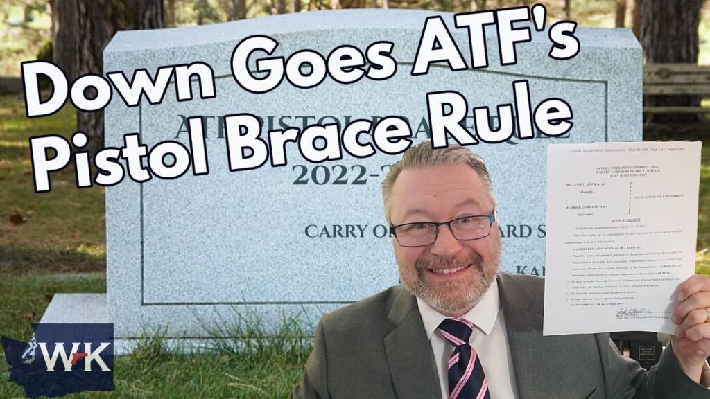 A man in a suit and tie holds up a document, smiling. Behind him is a large tombstone with the text "Down Goes ATF's Pistol Brace Rule" and dates 2022-2023. The initials "WK" are in the bottom left corner.