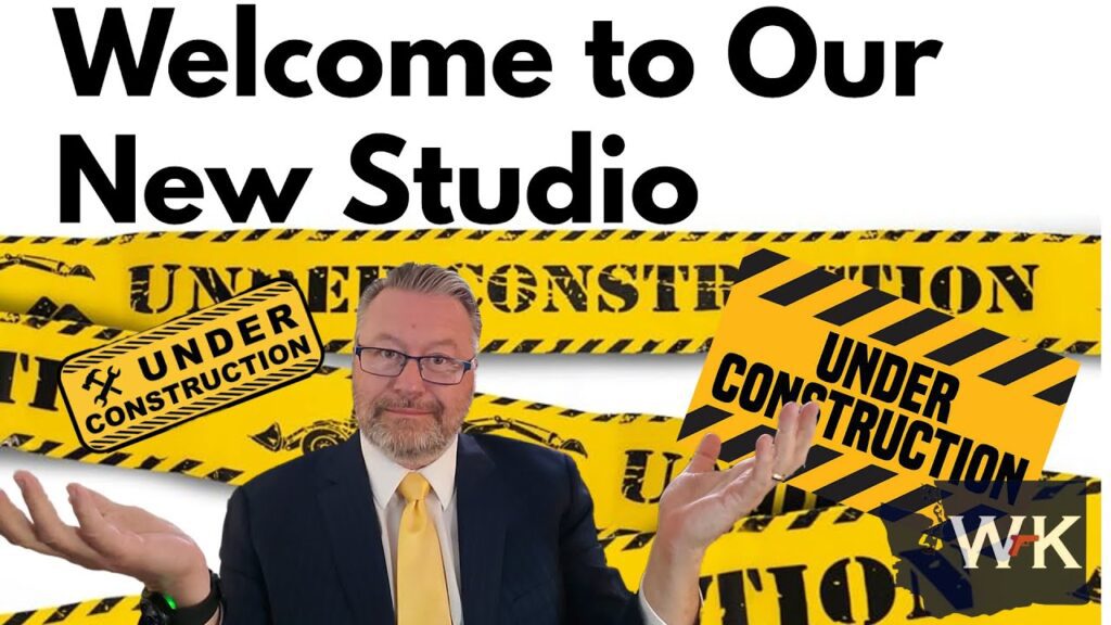 Man in a suit and yellow tie stands with arms outstretched in front of yellow and black "Under Construction" signs. The background features "Welcome to Our New Studio" text and caution tape.