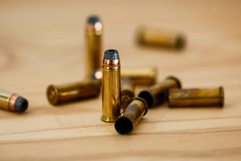 Close-up of several brass bullets with copper tips scattered on a wooden surface. One bullet is upright and in focus, with others blurred in the background.