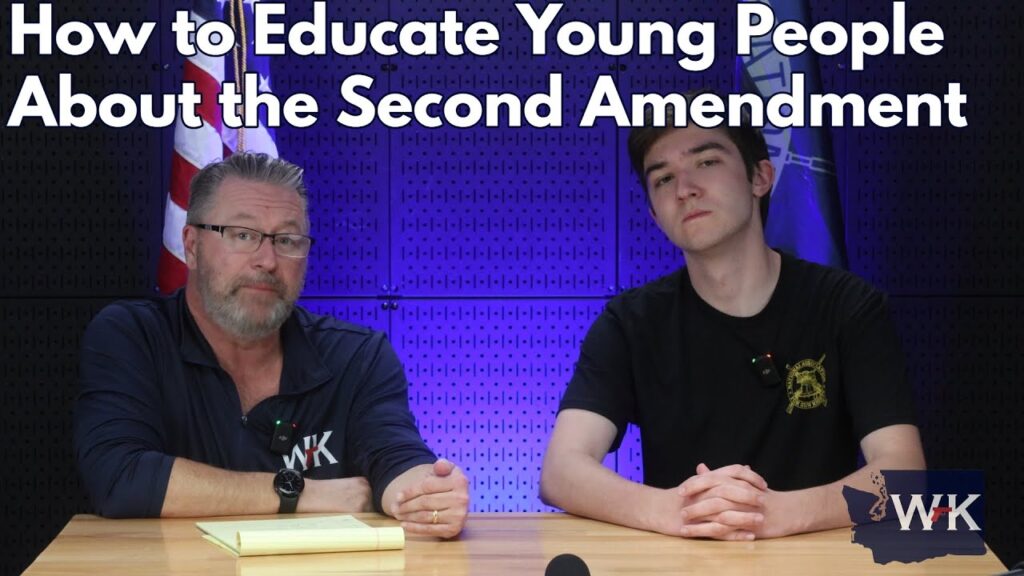 Two people are sitting at a table with microphones, discussing the topic "How to Educate Young People About the Second Amendment." The background features a dark patterned wall with a flag partially visible.