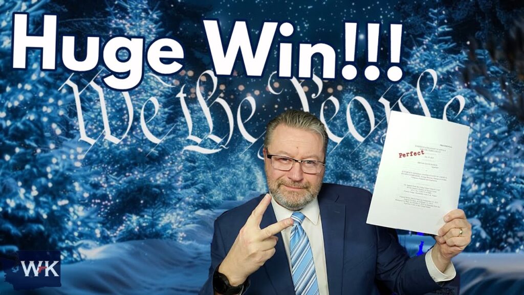 A man in a suit holds up a sheet of paper with "Perfect" written on it. He makes a peace sign with his other hand. The background has a holiday theme with trees and the words "We the People." Text reads "Huge Win!!!" at the top.