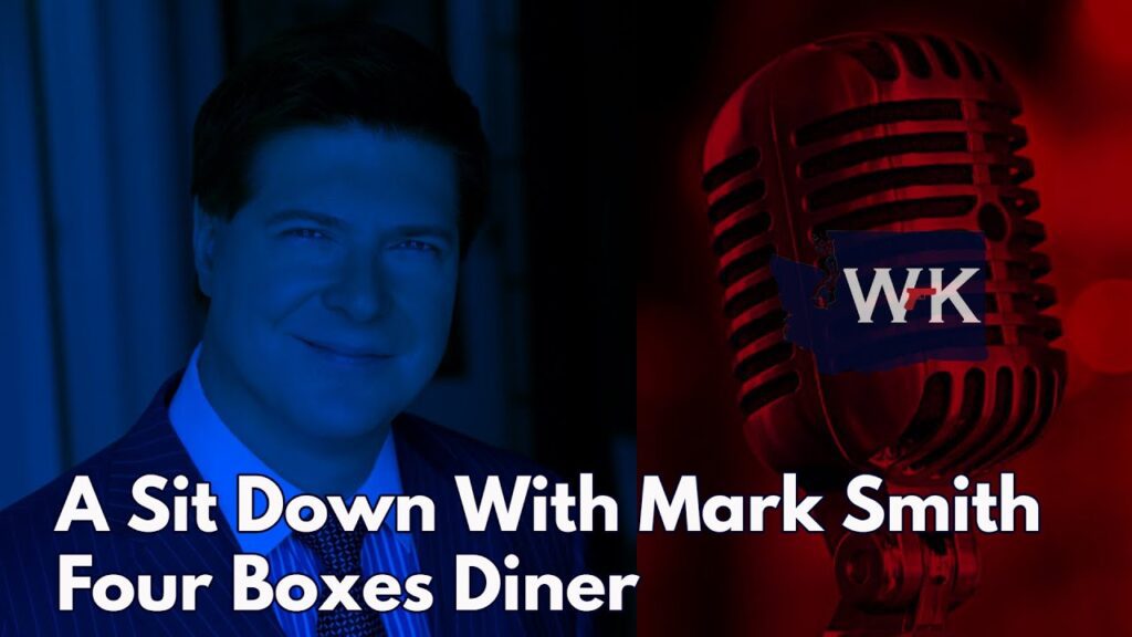 A blue-tinted portrait of a man in a suit is on the left, and a red-tinted vintage microphone with "WK" is on the right. Text reads: "A Sit Down With Mark Smith Four Boxes Diner.