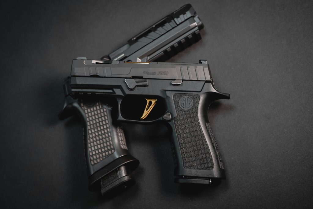 Two black semi-automatic pistols with textured grips are placed on a dark surface. One pistol is fully visible, while the second is partially visible, positioned on top of the first.