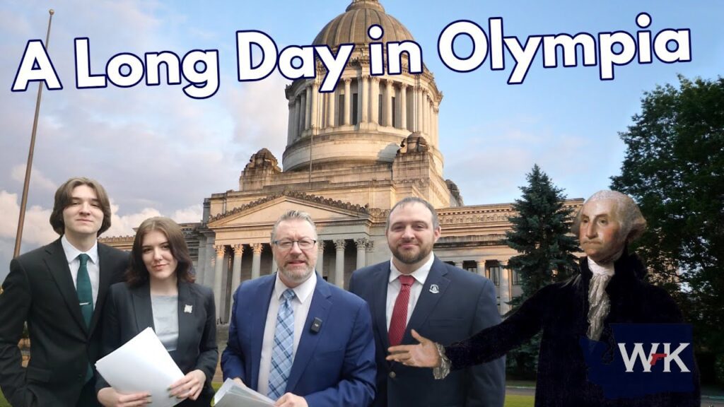 Four people in formal attire stand in front of a large domed building, with an illustration of a historical figure on the right. The sky is partly cloudy. Text on the image reads "A Long Day in Olympia.