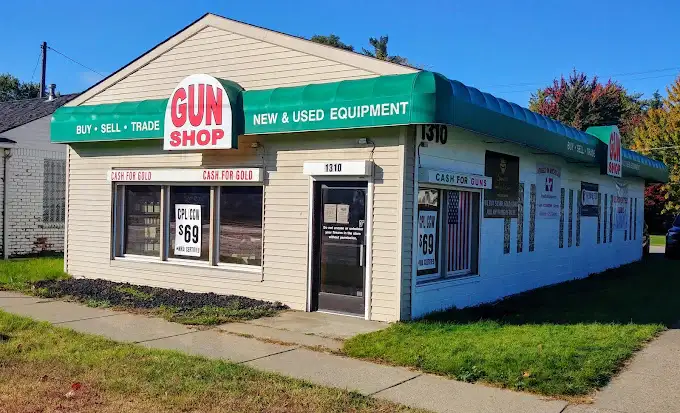 A beige building with a green awning labeled "Gun Shop" offers buying, selling, and trading services for new and used equipment. Signs advertise cash for gold and cash for guns. The storefront has large windows and a door with a sign on it.