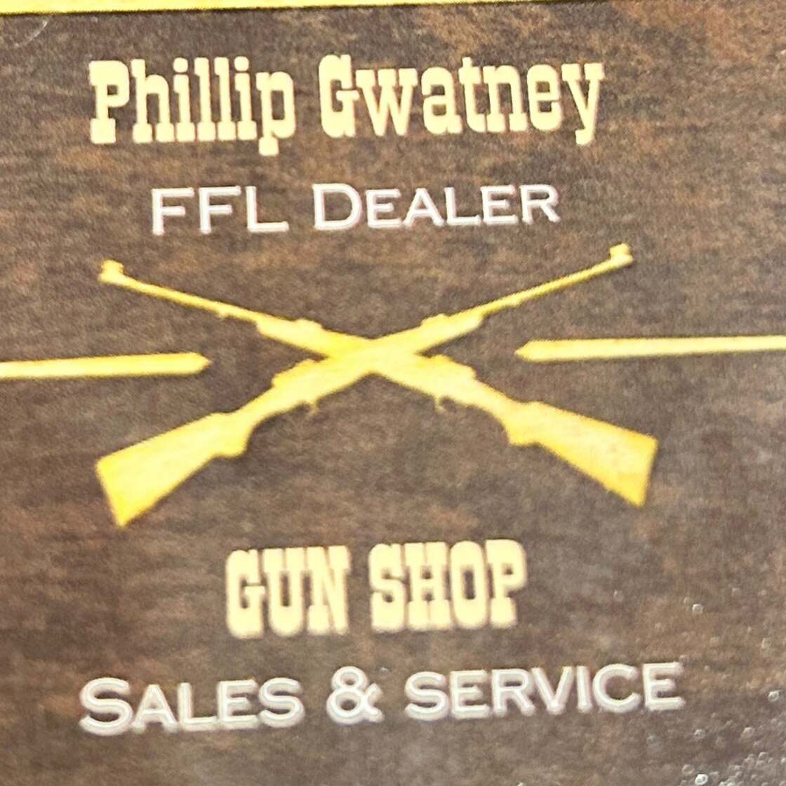 Image of a sign for "Phillip Gwatney FFL Dealer Gun Shop" in white text on a brown background. Two crossed rifles are depicted above the words "Sales & Service." The overall design has a rustic appearance.