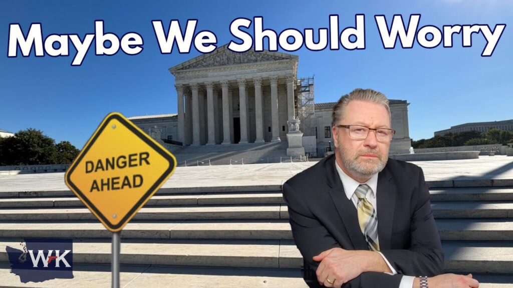Man in a suit poses in front of a large building with columns, with a road sign reading "Danger Ahead" beside him. Text above reads "Maybe We Should Worry." The sky is clear and blue.