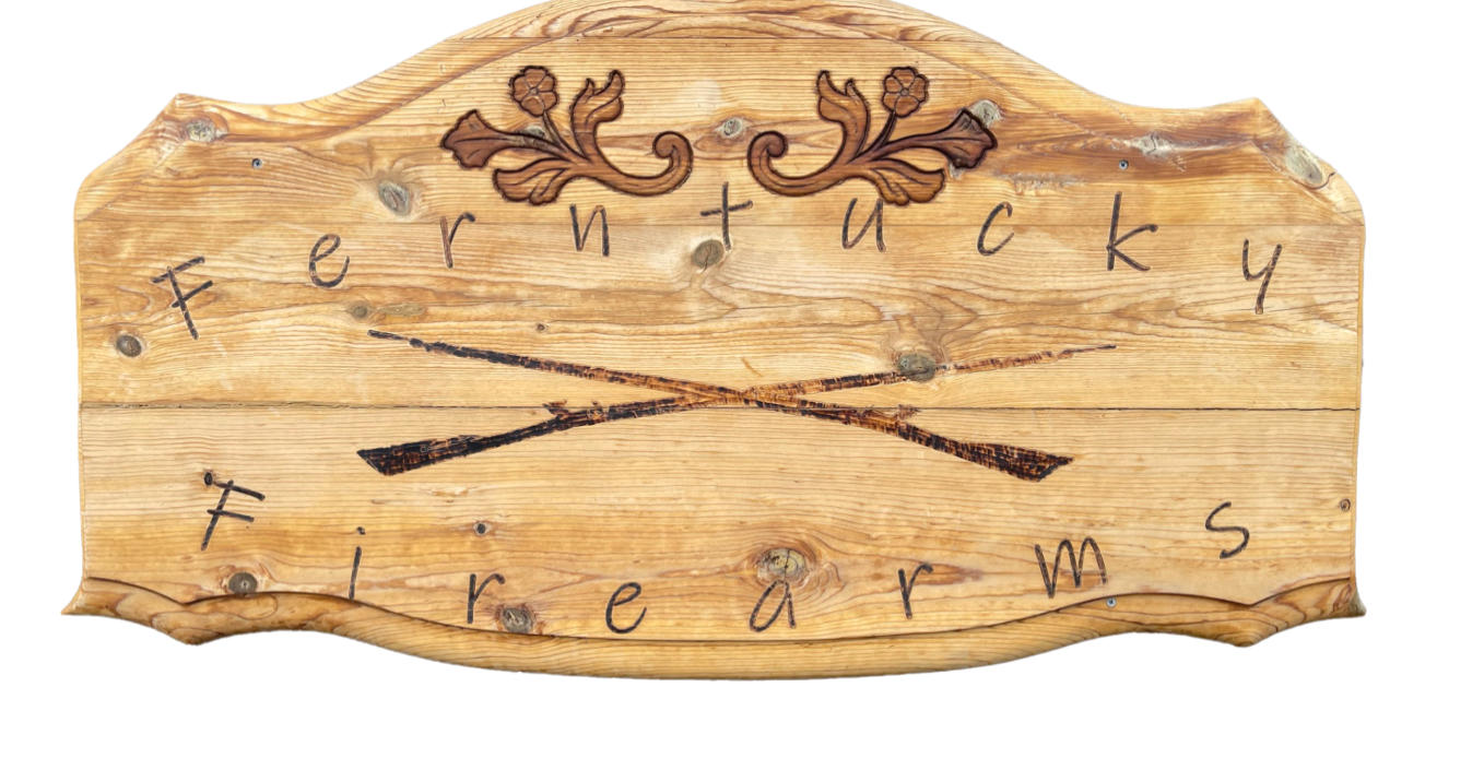 A wooden sign with engraved floral designs at the top and the words "Ferntucky Firearms" in a handwritten style, featuring two crossed rifles in the center.
