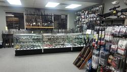 A gun shop interior with glass display cases showcasing various firearms. Rifles are mounted on the walls, and shelves display ammunition and accessories. Bright fluorescent lighting illuminates the space.