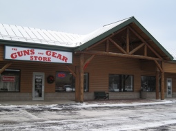 Single Category 4 A wooden storefront with a large sign reading "The Guns and Gear Store" above the entrance; snow is on the ground in front of the building.
