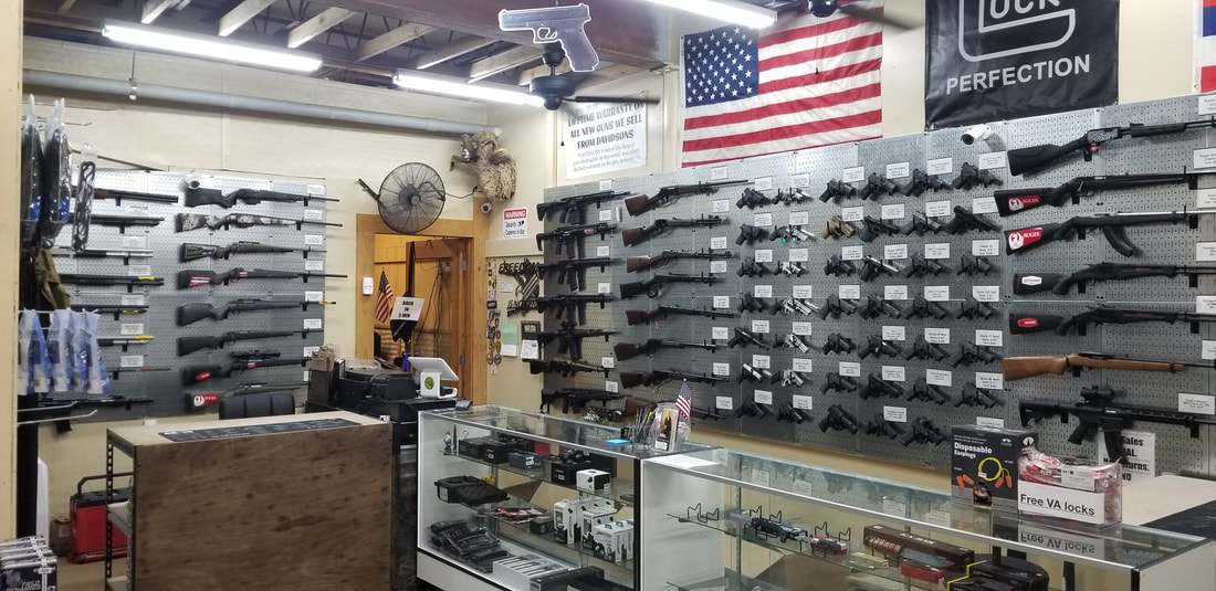 A gun store interior features multiple rifles and handguns displayed on pegboards. A glass counter showcases various accessories. An American flag and a large Glock poster hang on the wall. The store has a rustic wooden ceiling and cluttered decor.