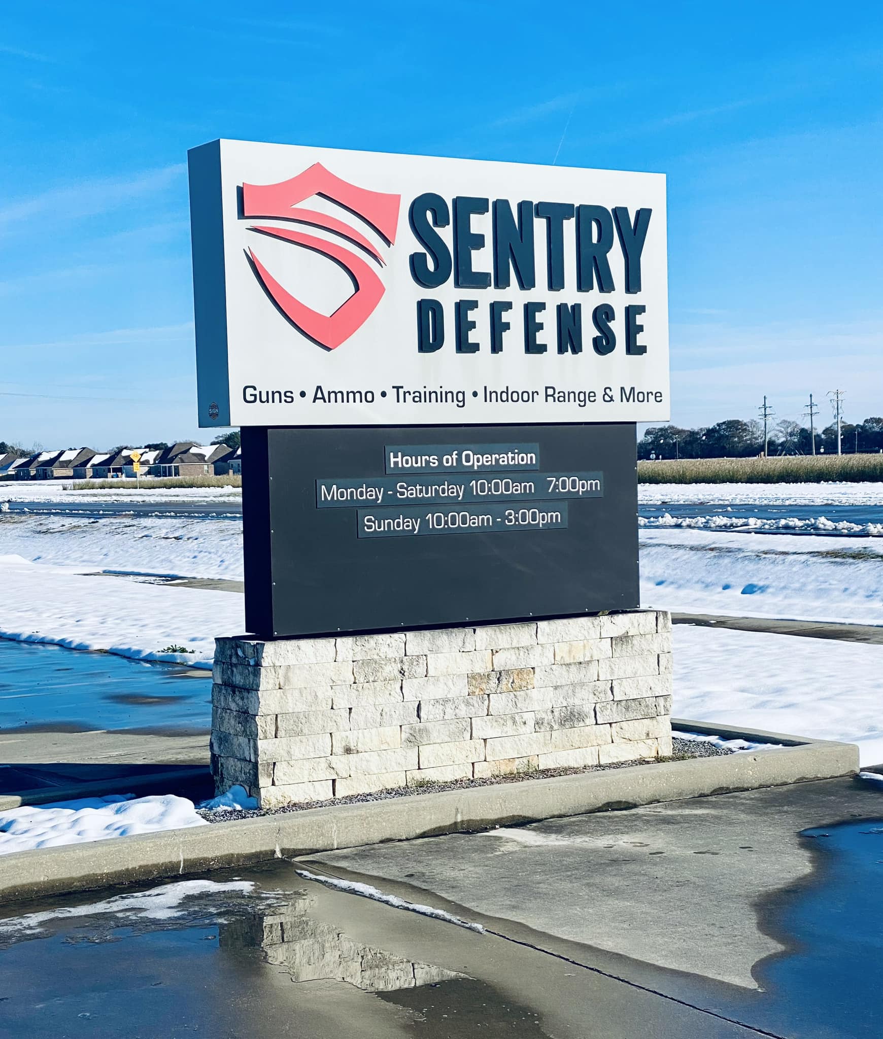 A sign for Sentry Defense, advertising guns, ammo, training, an indoor range, and more. The hours of operation are Monday–Saturday 10:00am–7:00pm, and Sunday 10:00am–3:00pm. Snow is on the ground nearby.