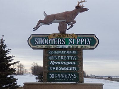 Shooting Range Directory 17 A large outdoor sign for "Midwestern Shooters Supply" features a deer statue on top and advertises guns, ammo, reloading, archery, and fishing brands including Leupold, Beretta, Remington, Browning, and Federal Premium.