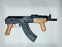 Single Category 1 A compact assault rifle with a wooden foregrip and pistol grip, black metal body, and curved magazine, displayed against a plain light background.