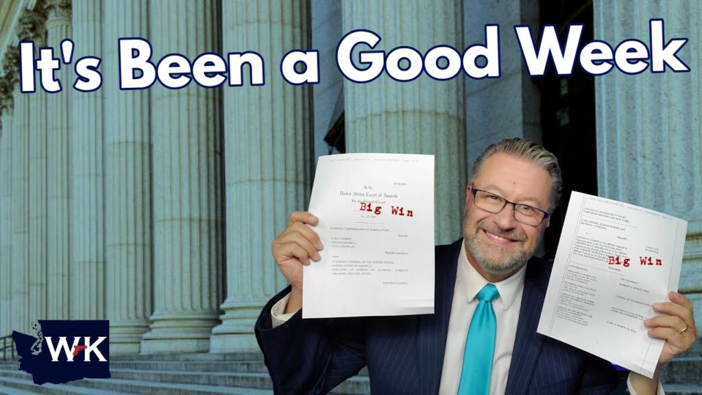 A smiling man in a blue suit and tie holds up two documents labeled "Big Win" in red text, standing in front of large courthouse columns. The text above reads "It's Been a Good Week.