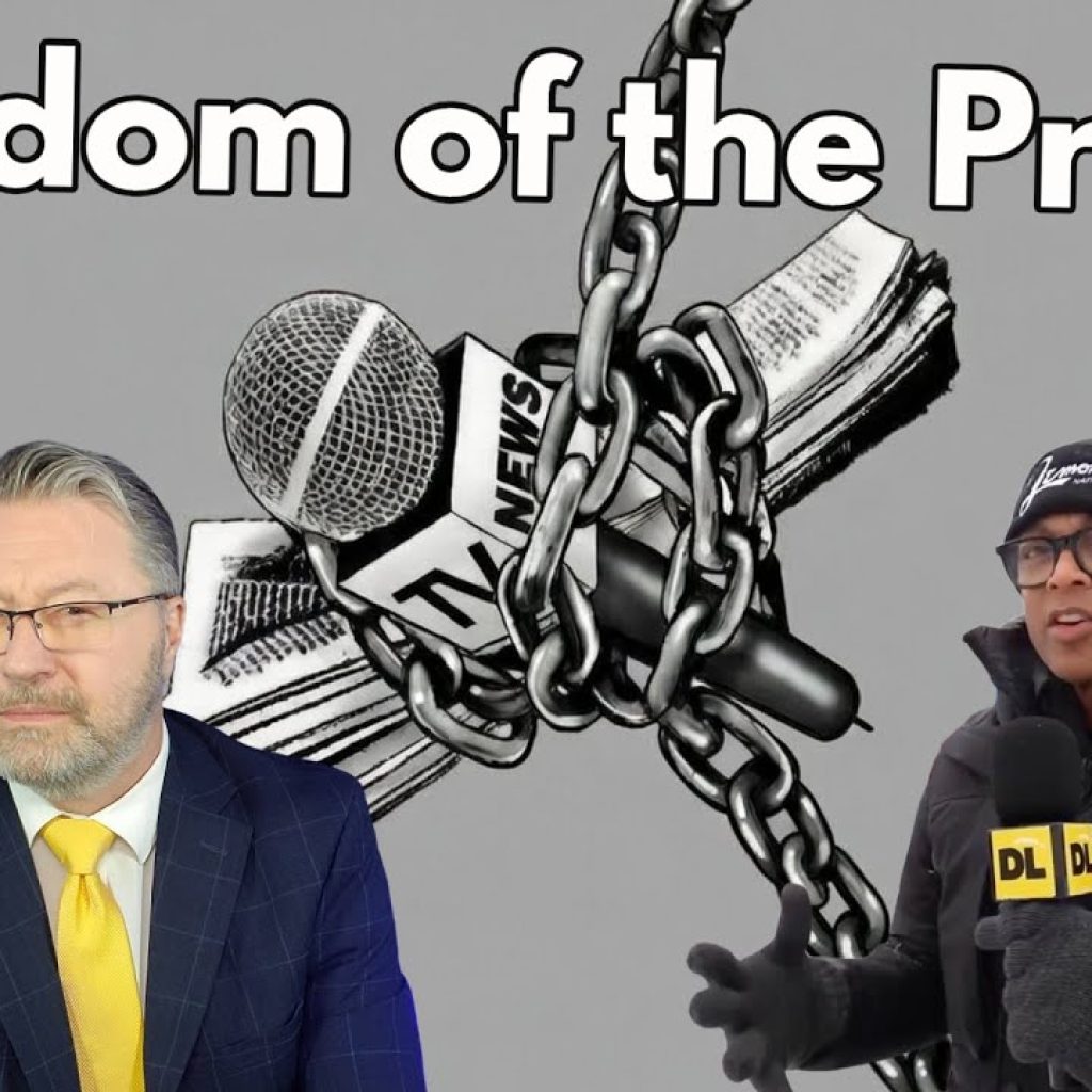 Two men stand in front of an illustration of a TV news mic and newspaper wrapped in chains; large text reads “Freedom of the Press?” The left man wears a suit, the right is bundled for cold weather, holding a DL mic.