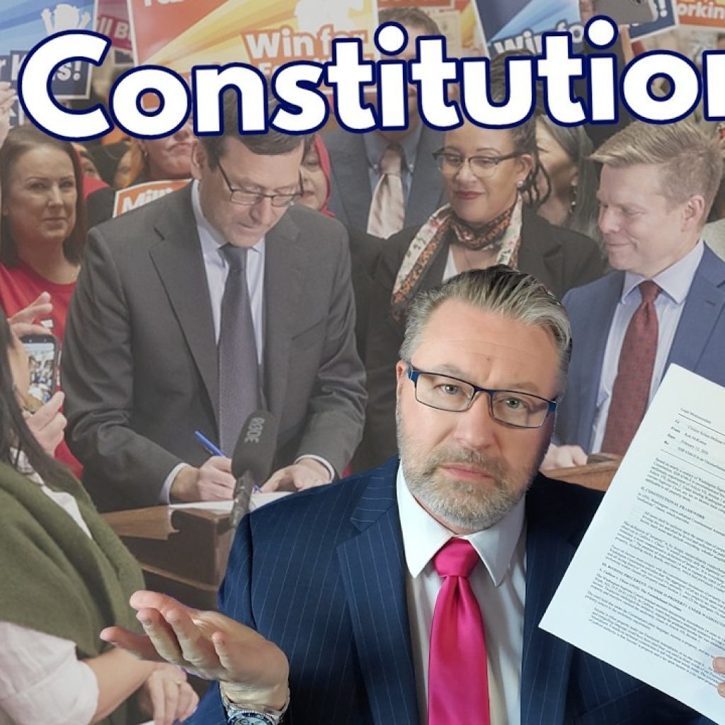 A man in a suit and glasses shrugs while holding documents. Behind him, people hold signs reading "Millionaires Tax is a Win" and "Winning for Working Families" with "Is It Constitutional?" in large text above.